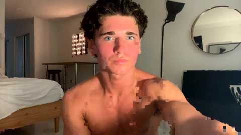 Media: A video of a shirtless young man with short, dark hair, blue eyes, and a youthful, lean physique, taken in a modern, minimalist bedroom with a bed, mirror, and dim lighting.