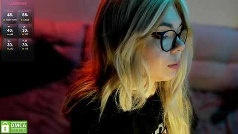 Media: Video of a young woman with long, blonde hair, wearing black glasses and a black top, indoors with blurred background, and a \"DCA Productions\" watermark.