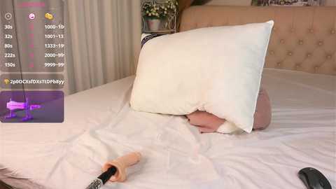 Media: Video of a baby lying on a white bed, partially covered by a white pillow, with a plush toy and a remote control nearby.