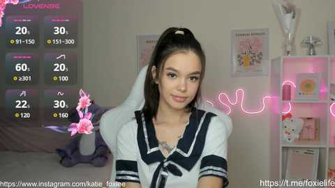 Media: Video of a young woman with long black hair, wearing a white sailor schoolgirl outfit, standing in a pink-lit room with a digital thermometer and posters on the wall.