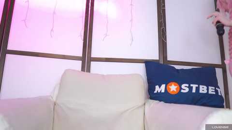 Media: Video of a cozy living room with a cream sofa and a blue pillow with \"MOSTBETEN\" in white and orange text.