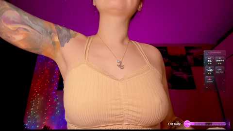 Media: Video of a light-skinned woman with tattoos on her arm, wearing a beige ribbed tank top, standing in a dimly lit room with purple and red lighting.