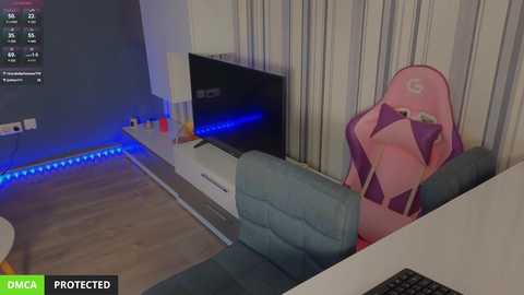 Media: Video of a modern, minimalist living room featuring a pink gaming chair, blue LED lighting, and a flat-screen TV.