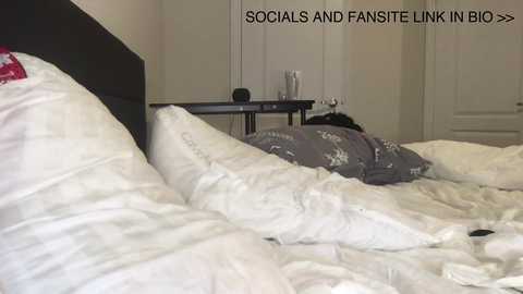 Media: Video of a messy bedroom with white bedsheets, a gray duvet, and a black headboard. A white door is in the background. Text overlays: \"SOCIALS AND FANSITE LINK IN BIO.\