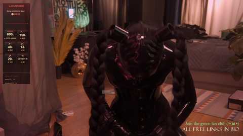 Media: Video of a muscular, dark-skinned man in a latex suit, standing in a dimly lit room with a bed and potted plants, wearing a virtual reality headset.