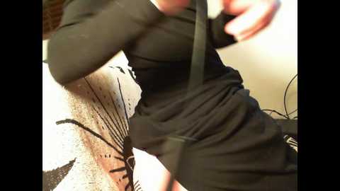 Media: A close-up video of a person wearing black clothing, adjusting a strap, with a blurred background featuring a white and brown textured fabric.