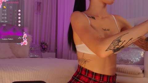 Media: Video of a woman with long black hair, tattoos, wearing a white bra, red plaid skirt, in a purple-lit bedroom with a bed and digital avatar.