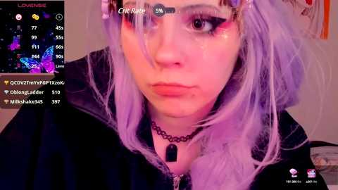 Media: Video of a young woman with light skin, lavender hair, wearing a black hoodie and choker, with a livestream overlay showing viewers and chat.