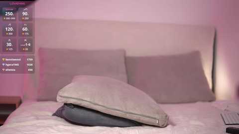 Media: Video of a minimalist bedroom with a beige headboard and two pillows in shades of grey, featuring a digital screen displaying temperature, humidity, and air quality data.