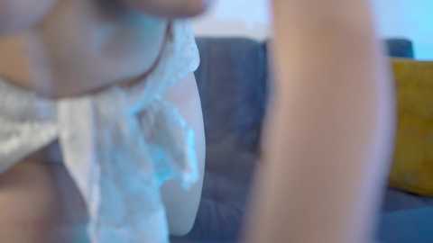 Media: A blurred video showing a woman in a white, see-through lingerie top, with her breasts partially visible, and a yellow pillow in the background.