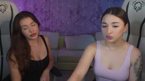 Media: Video of two young women in a dimly lit room, one with long brown hair in a black top, the other with short hair in a light pink tank top.