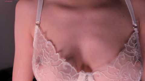 Media: Close-up video of a fair-skinned woman in a delicate, white lace bra, with visible cleavage, and shoulders partially in focus.