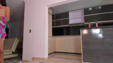 Media: A video of a modern kitchen with light wooden cabinets, black countertops, and a woman in a colorful swimsuit standing by the entrance.