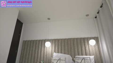 Media: Video of a minimalist bedroom with white walls, a gray headboard, two round white lamps, and white curtains.