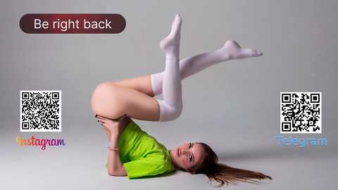 Media: Video of a slender, fair-skinned woman with long brown hair, wearing a green T-shirt and white thigh-high socks, performing a headstand, with a \"Be Right Back\" text overlay and \"Telegram\" branding.