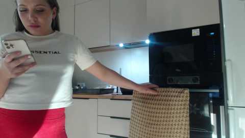 Media: Video of a woman in a white shirt and red skirt, holding a woven basket, in a modern kitchen with white cabinets and a black oven.