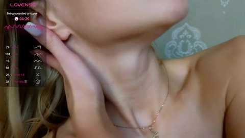 Media: Video of a topless woman with light skin and long, blonde hair, partially obscuring her face. She is wearing a thin gold necklace. The background shows a blurred, ornate wallpaper.