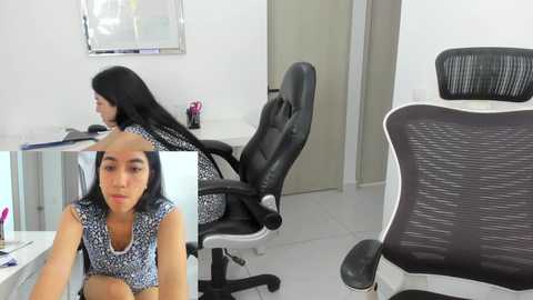 Media: Video of a modern office with a woman in a blue patterned dress sitting at a desk, and a black mesh ergonomic chair in the foreground.