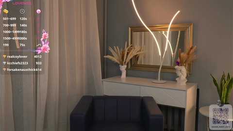 Media: Video of a modern, minimalist bedroom featuring a white dresser with a mirrored frame, white vase with dried flowers, and a dark blue armchair.