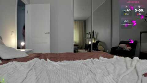 Media: Video of a modern, well-lit bedroom with a neatly made bed, a large mirror reflecting the room's interior, and a cozy armchair.