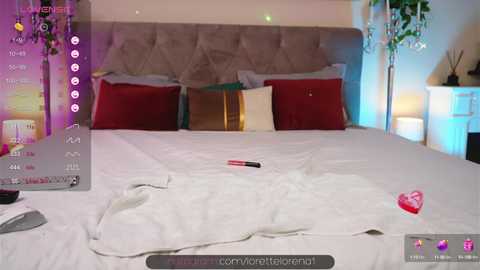 Media: A video of a cozy bedroom with a plush bed adorned with white sheets, red pillows, and a heart-shaped chocolate on the bedspread. The room features a tufted headboard, a nightstand, and soft lighting.