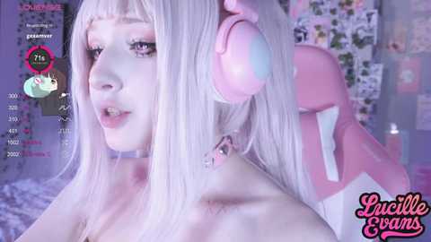 Media: A soft-focus video of a pale-skinned woman with long, platinum blonde hair, wearing pink headphones and a choker, set against a pastel pink and white background.