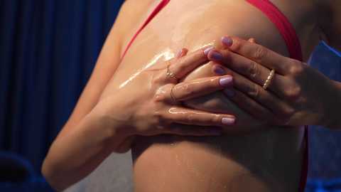 Media: Video of a light-skinned woman with wet, glistening skin, wearing a red bra. She has manicured nails painted lavender and is pressing her hands against her bare back, creating a sensual, intimate atmosphere.