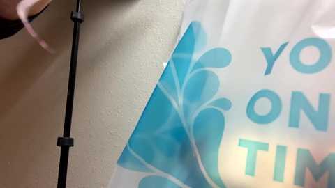 Media: A close-up video of a white wall with a partially visible blue and white floral patterned banner. The banner features the words \"You Are On Time\" in bold blue text. The background includes a black microphone stand.