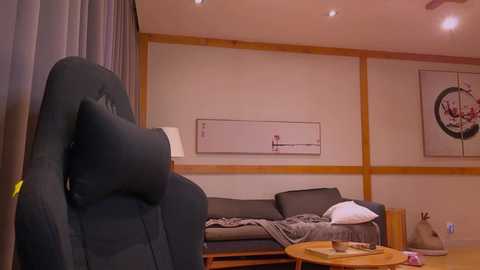 Media: Video of a modern, minimalist living room with a black leather recliner, gray sofa, wooden floor, and abstract wall art.