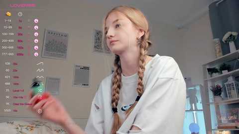 Media: Video of a young, fair-skinned woman with long blonde braids, wearing a white t-shirt, holding a green bottle in a modern, brightly lit room.