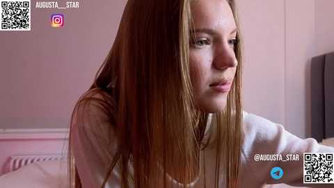 Media: Video of a young, fair-skinned woman with long, straight, light brown hair, wearing a white top, looking contemplative in a softly lit, pink-toned bedroom. QR codes and social media icons are visible in the corners.