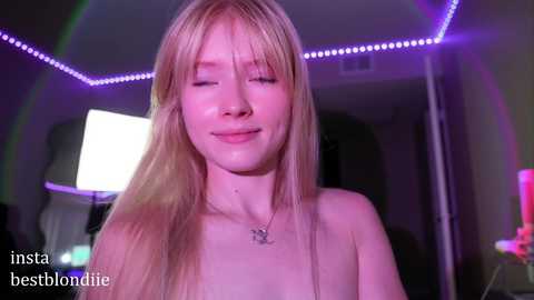 Media: Video of a young, topless, fair-skinned blonde woman with long hair, smiling, in a dimly lit room with purple LED strip lights, blurred background, watermark \"insta bestblondie\" in the corner.