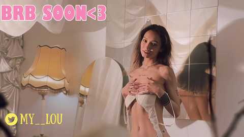 Media: Video of a slim, nude woman with light skin and long, wavy brown hair, covering her breasts with her hands. Background features a mirrored wall, a yellow lamp, and a white chair. Text reads \"BRR S00K\" in pink.