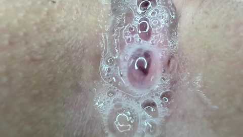 Media: Video of a close-up, intimate view of a woman's vulva, with a focus on the labia majora and labia minora, featuring light brown skin and visible vaginal fluids with bubbles.