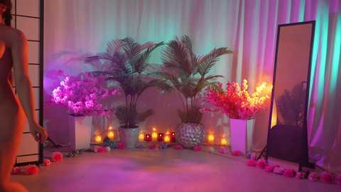 Media: Video of a serene, softly lit room with pink, purple, and white floral arrangements, candles, and a standing mirror, creating a tranquil, romantic ambiance.