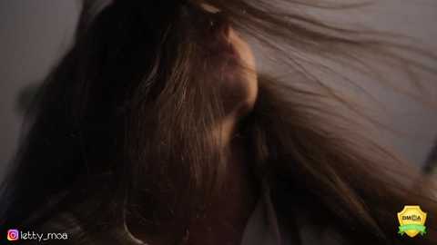 Media: A close-up video of a woman's head, with long, straight, dark hair partially obscuring her face. Her skin tone is light, and she has a serene expression. The background is blurred, emphasizing the hair texture.