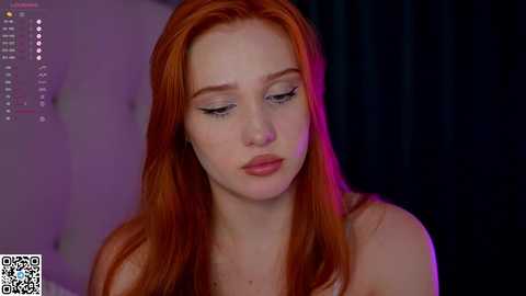 Media: A video of a fair-skinned woman with long, vibrant red hair, wearing minimal makeup, with a pensive expression. She has a slender build and is wearing a sleeveless top.