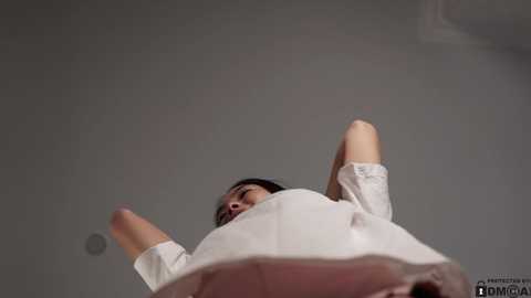 Media: Video of a young woman in a white dress, arms raised, looking upward, against a plain gray background.