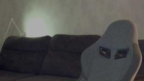 Media: A dimly lit video of a beige recliner chair with a light glowing behind it, set against a plain, light-colored wall. The chair's backrest features a small, reflective surface with a mirrored design.