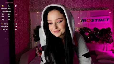 Media: Video of a smiling young woman with long black hair in a Star Wars-themed hoodie, standing in a dimly lit bedroom with pink and purple lighting, Christmas decorations, and a \"MOSTBEAUTIFUL\" poster in the background.