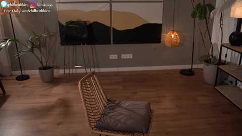 Media: Video of a modern, minimalist living room with a woven chair, potted plants, abstract art on the wall, and warm wooden flooring.