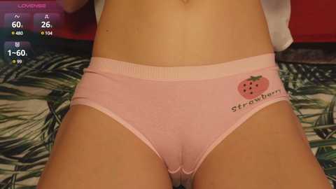 Media: A video of a woman wearing pink panties with a strawberry graphic, lying on a bed with green and white floral sheets.