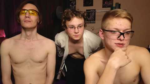 Media: Video of three shirtless young men in a dimly lit room. One has yellow-tinted glasses, one is wearing glasses, and the third is touching his chin thoughtfully.