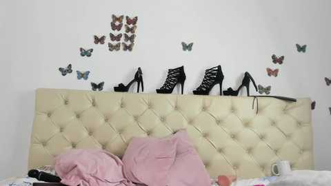 Media: A video of a bed with a cream tufted headboard, pink sheets, and black high heels arranged on the wall, surrounded by butterfly stickers and a white mug.