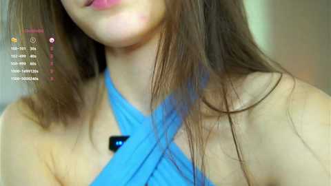 Media: Video of a young woman with long brown hair, wearing a blue halter top, partially cropped. Her face is out of frame.