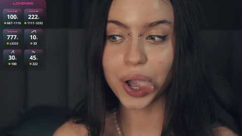 Media: Video of a woman with long black hair, light skin, and full lips, licking her tongue. The background is dark, with a screen displaying \"Loud House\" and game statistics.