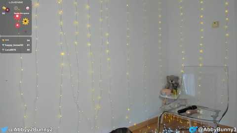 Media: A video showing a cozy, minimalist room with a clear plastic chair, a small table, and string lights. The room is bright, with a soft yellow glow from the lights.