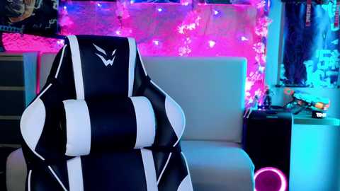 Media: A video of a black-and-white striped gaming chair with a white logo in a neon-lit room with multicolored fairy lights, a white couch, and various gaming accessories.