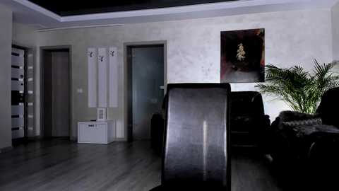 Media: Video of a minimalist, dimly-lit living room with a black television, white furniture, and abstract artwork on a textured beige wall.