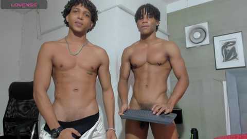 Media: Video of two shirtless young men with dark skin, one with short dreads and the other with a buzz cut, standing in a modern office setting.